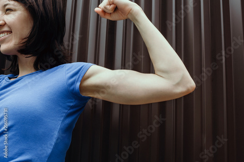 Smiling woman flexing her biceps outdoors, selective focus