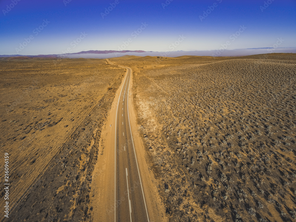 Rural road passing through dry land with scarce vegetation at sunrise  - aerial panorama