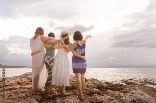 Summer lifestyle of four pretty women having fun and relax on beach. Point to copy space. Summer concept. Cinema film tone with grain.