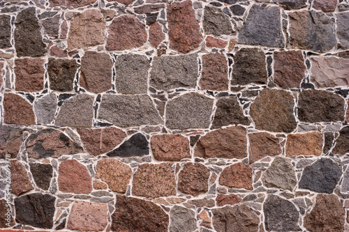 Wall of stones. Stones of different shapes and colors. The mortar connecting the masonry is white. Well suited as a background or texture