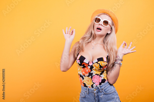 Cool beautiful young woman wearing eyewear glasses, in studio with hat over yellow background