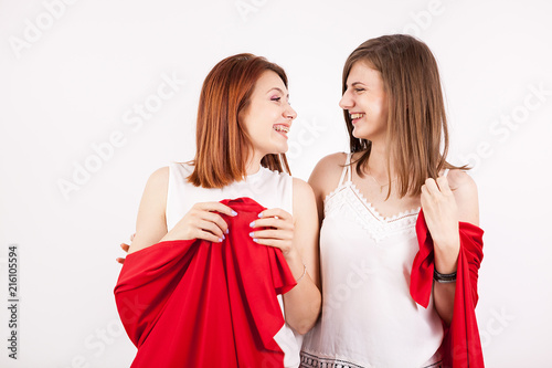 Two beautiful female friends covering them self with a red blanket in studio photo over a white wall