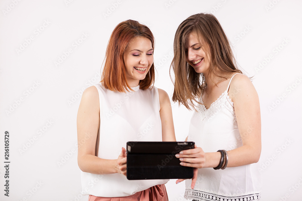 Portrait of two gorgeous women holding a tablet PC and looking at it while smiling Portrait of two gorgeous women holding a tablet PC and looking at it while smiling