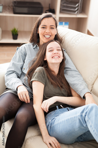 The oldes sister is cuddling the younger one on the couch in the living room photo