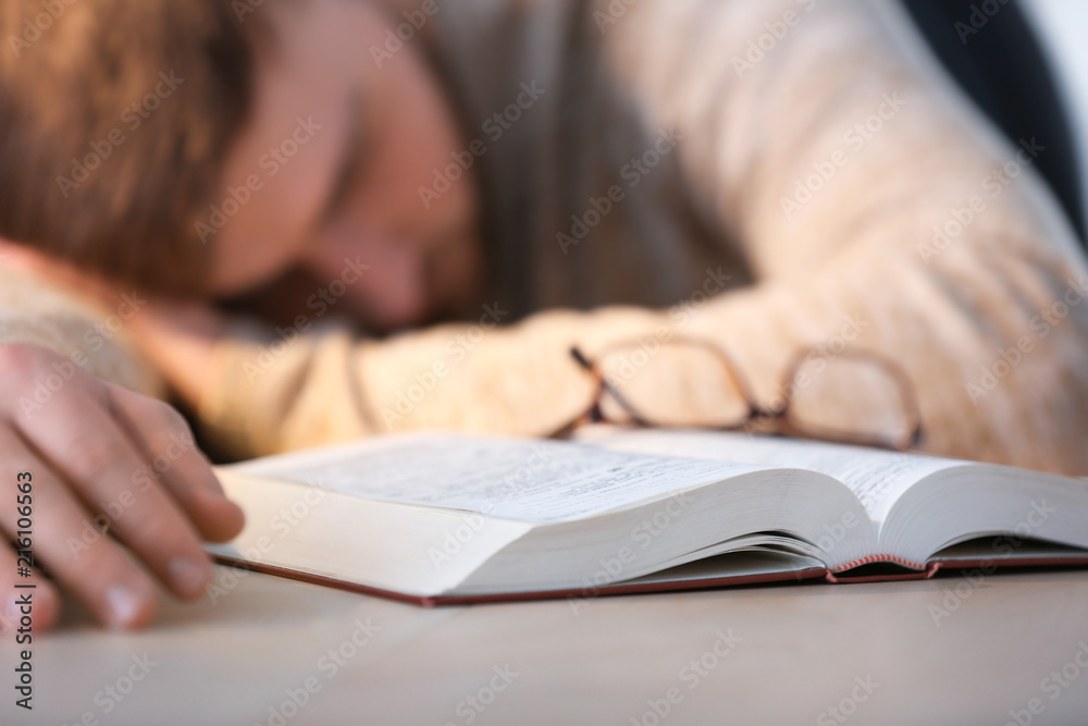Tired young man sleeping at table with book Tired young man sleeping at table with book