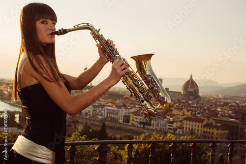 Young brunette girl playing sax outdoor having the famous Florence dome as background