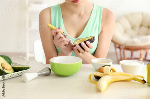 Woman making nourishing mask with avocado in kitchen
