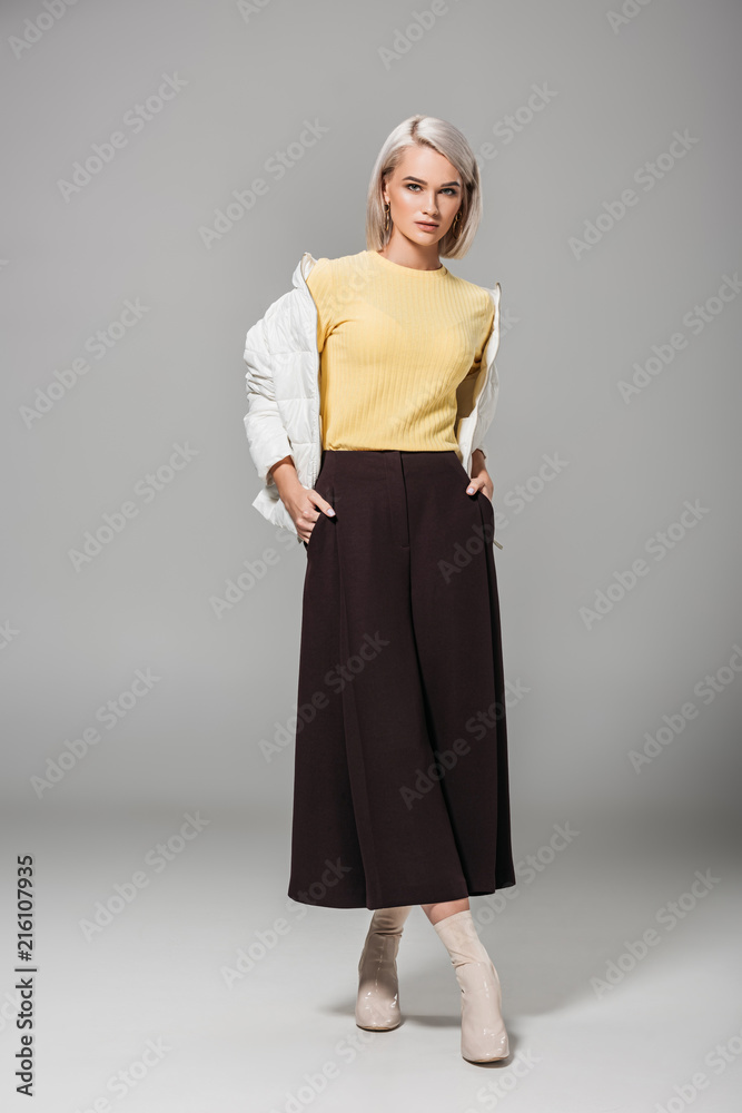 serious young female model in stylish autumn outfit posing with hands in pockets on grey background serious young female model in stylish autumn outfit posing with hands in pockets on grey background