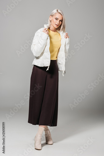 attractive female model in stylish white jacket posing on grey background