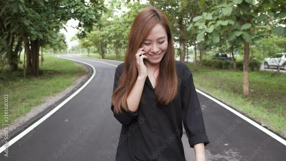 A woman talking on a phone while walking on the road with green nature background A woman talking on a phone while walking on the road with green nature background