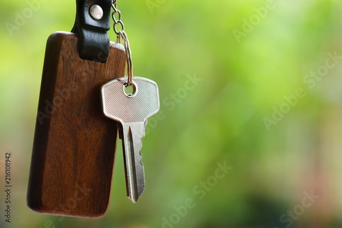 House keys with wooden home keyring with green garden background, property concept, copy space