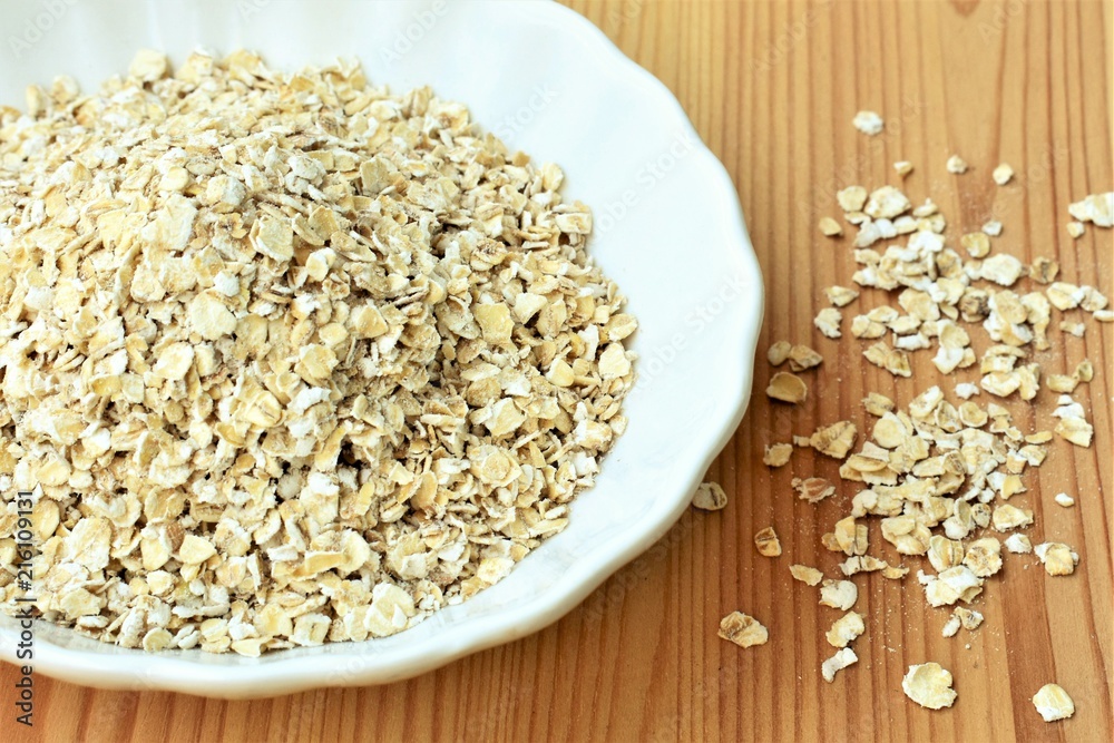 Oat flakes uncooked, in a white bowl, on a wooden table. Oat flakes uncooked, in a white bowl, on a wooden table.