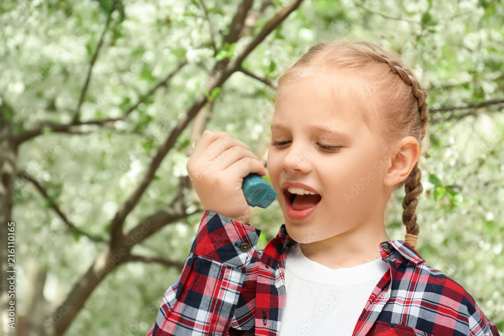 Little girl using inhaler near blooming tree. Allergy concept Little girl using inhaler near blooming tree. Allergy concept