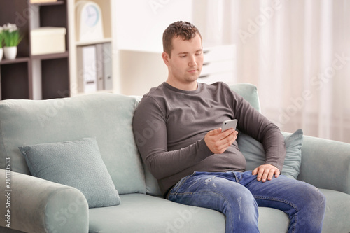 Young man using phone while resting on sofa at home