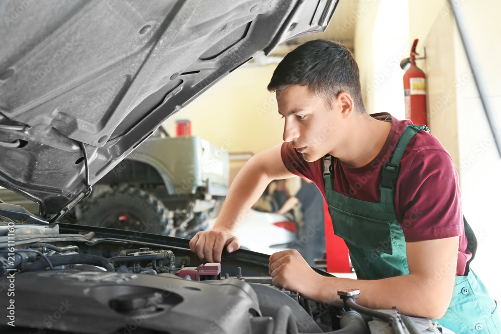 Young auto mechanic repairing car in service center