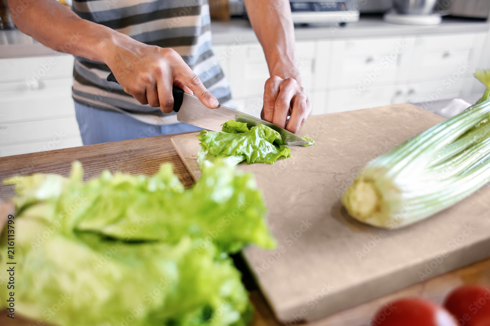 Young African-American man cutting salad in kitchen