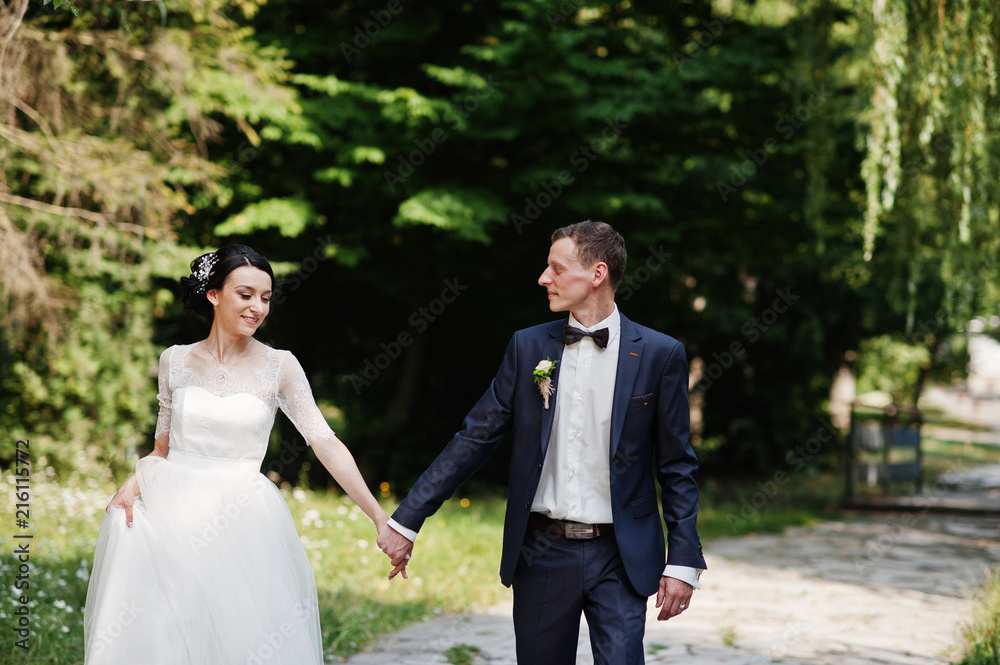 Gorgeous wedding couple holding hands and walking in the park on the sunny day.