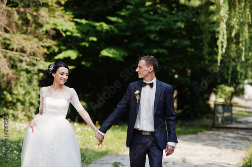 Gorgeous wedding couple holding hands and walking in the park on the sunny day.