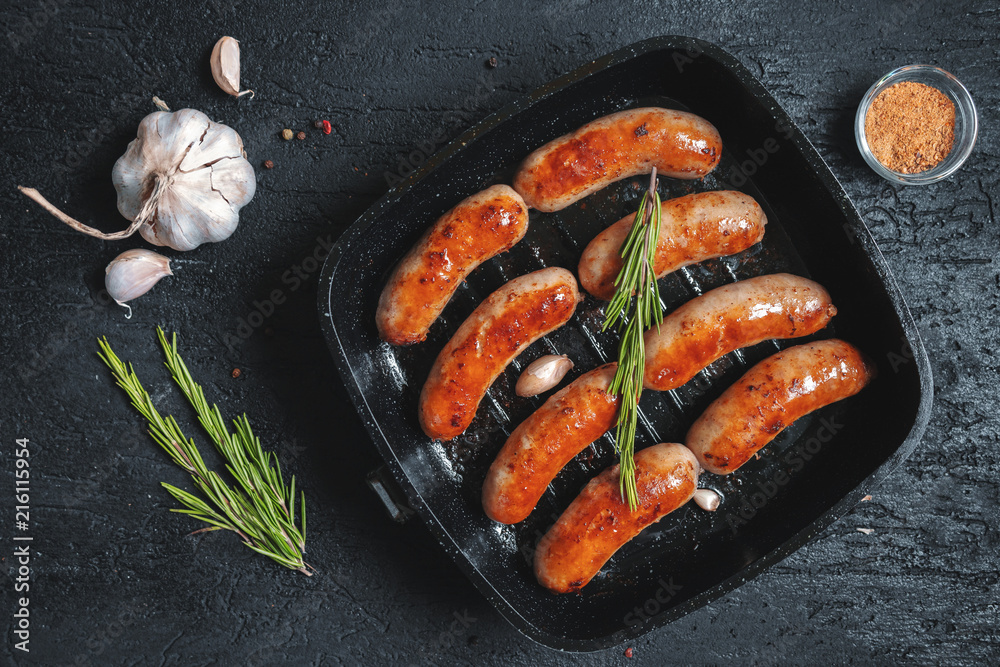 Top view on fried sausages in a black frying pan on a black stone table