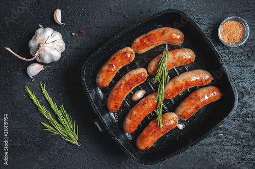 Obraz na płótnie Top view on fried sausages in a black frying pan on a black stone table w salonie