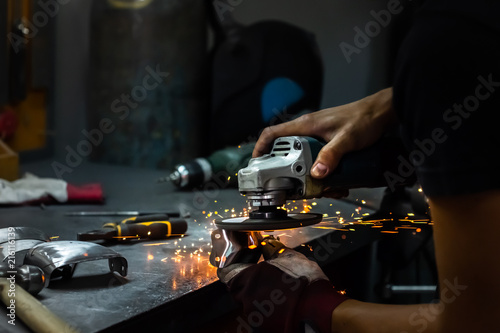 Male metal worker polishing and finalising piece of medieval armour suit. Man hands treating metal parts of hardware in a workshop with angle grinder photo