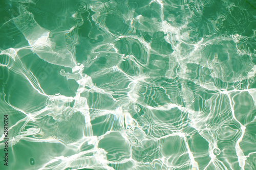 Green water surface with bright sun light reflections, water in swimming pool background closeup