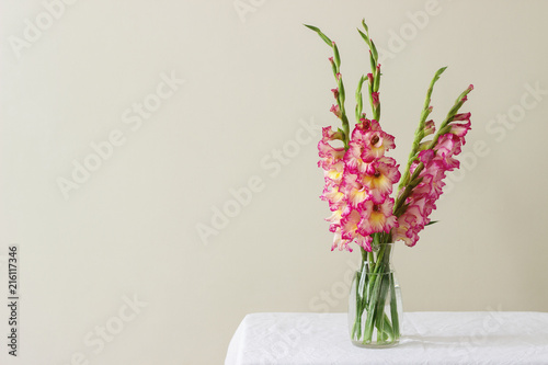 Obraz na płótnie A bouquet of multicolored gladioli in a glass vase on a light background. Greeting card. w salonie