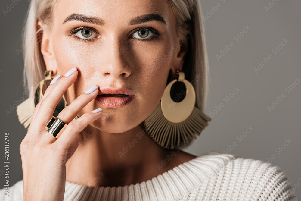attractive blonde girl posing in white sweater and big round earrings, isolated on grey - obrazy, fototapety, plakaty 