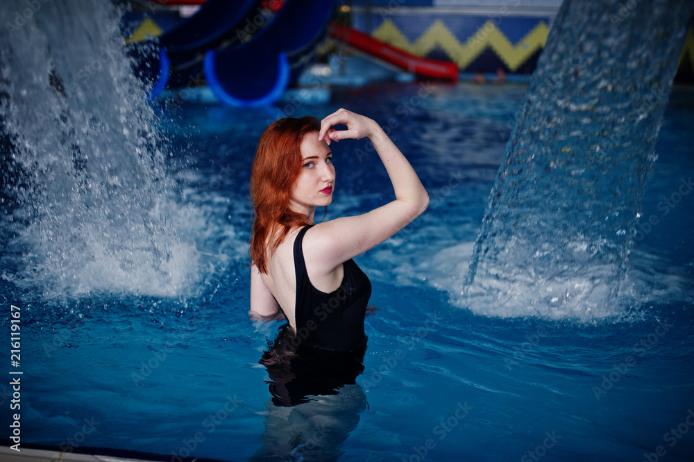 Obraz premium Sexy red haired girl in black swimsuit having rest in swimming pool of aqua park.