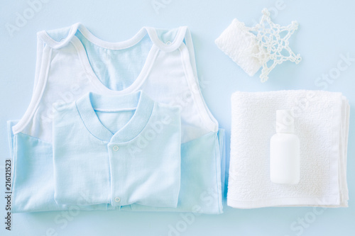 Light blue bodysuit on the pastel blue table in bathroom. White bottle of natural herbal shampoo on towel. Care about kids clean and soft hands, face, legs and body skin. Baby clothes. Soft colors.  © fotoduets