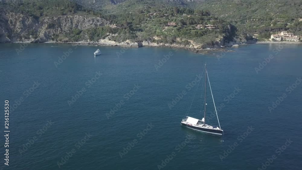 Aerial view of Tuscany rocky sea coast with boats at anchor above a turquoise sea with light reflections. People relaxing under the sun Aerial view of Tuscany rocky sea coast with boats at anchor above a turquoise sea with light reflections. People relaxing under the sun