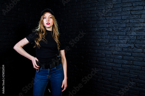 FBI female agent in cap and with gun at studio against dark brick wall. © AS Photo Family