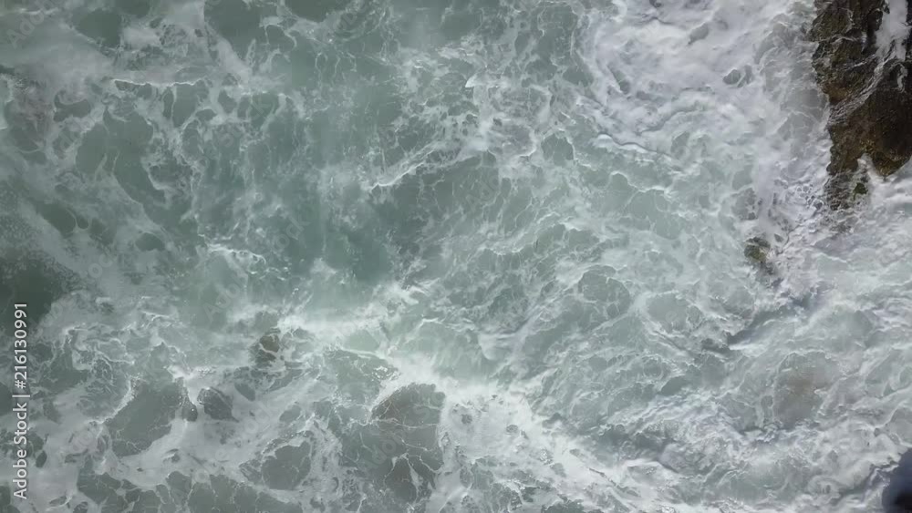 Aerial footage White foam of the waves between the rocks drawing a moving backgroud