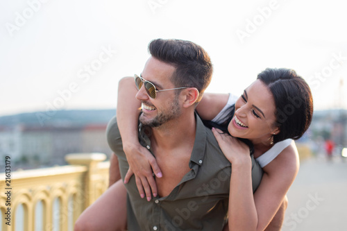 Happy young woman piggyback ride man outdoors in sunset