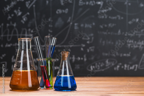 Fotografía Tubes with chemical liquids stand on a wooden table on a chalkboard background
