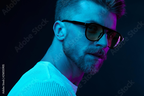 Neon light studio close-up portrait of attractive male model in sunglasses and white t-shirt