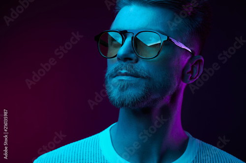 Neon studio portrait of serious man model with mustaches and beard in sunglasses and white t-shirt