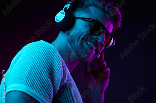 Neon light portrait of bearded smiling man in headphones, sunglasses, white t-shirt. Listening to music
