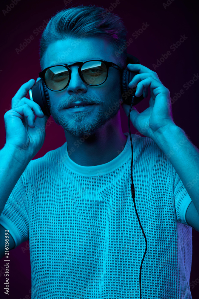 Handsome man in glasses enjoys listening to music with headphones. Neon studio portrait