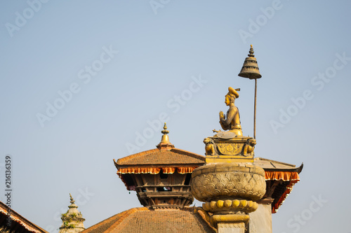 Durbar square in Bakhtapur, Nepal, with temple roofs and votive column with golden sitting figure under an umbrella. photo