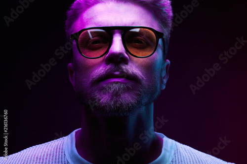 Neon light close-up portrait of serious man model with mustaches and beard in sunglasses and white t-shirt