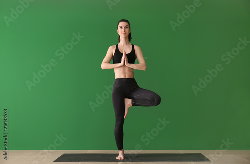 Young woman practicing yoga on near color wall