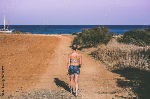 A woman is walking along the road to the sea in summer