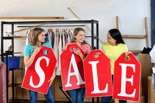 Beautiful young women with big tags composing word SALE in clothing shop photo