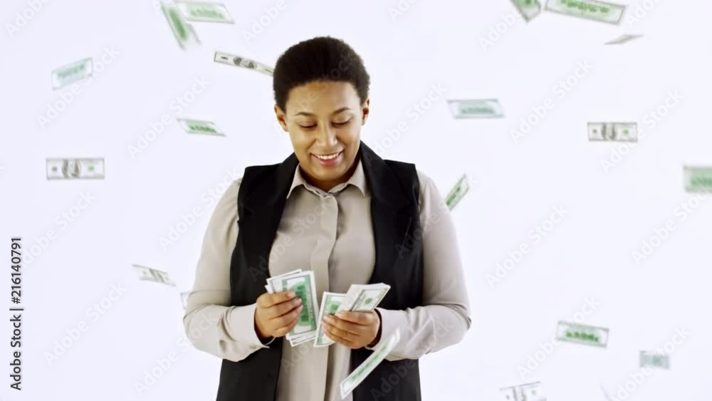 Slowmo studio shot of happy black businesswoman standing isolated on white background and counting cash as money falling down on her from above Slowmo studio shot of happy black businesswoman standing isolated on white background and counting cash as money falling down on her from above