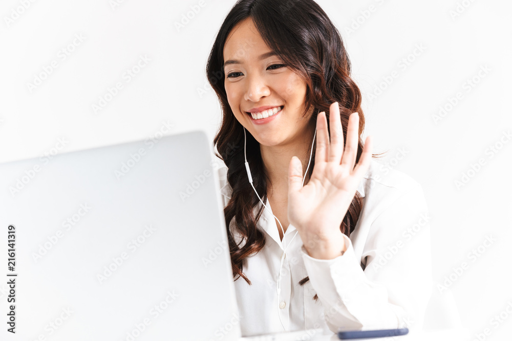 Photo of happy asian business woman 20s wearing office clothing waving at laptop, during video call or online conference, isolated over white background in studio Photo of happy asian business woman 20s wearing office clothing waving at laptop, during video call or online conference, isolated over white background in studio