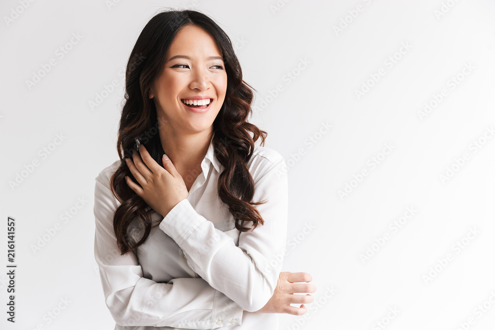 Fototapeta premium Image of charming chinese woman with long dark hair looking aside at copyspace and laughing, isolated over white background in studio