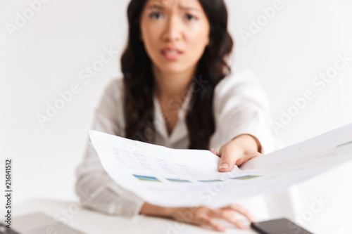 Blurry photo of tense asian woman employee with long dark hair holding and giving papers at camera while working in office, isolated over white background