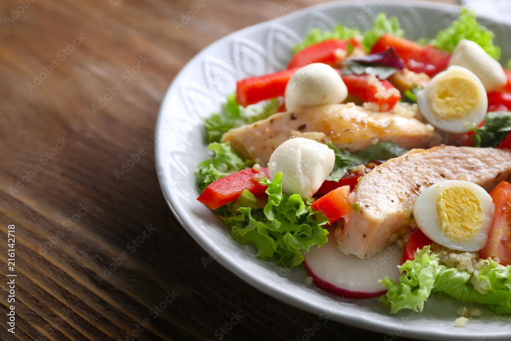 Tasty chicken salad with vegetables and quail eggs in bowl on wooden table Tasty chicken salad with vegetables and quail eggs in bowl on wooden table