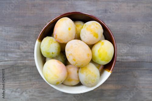 Ripe white plums in a clay bowl on a wooden table. Summer seasonal fruit concept